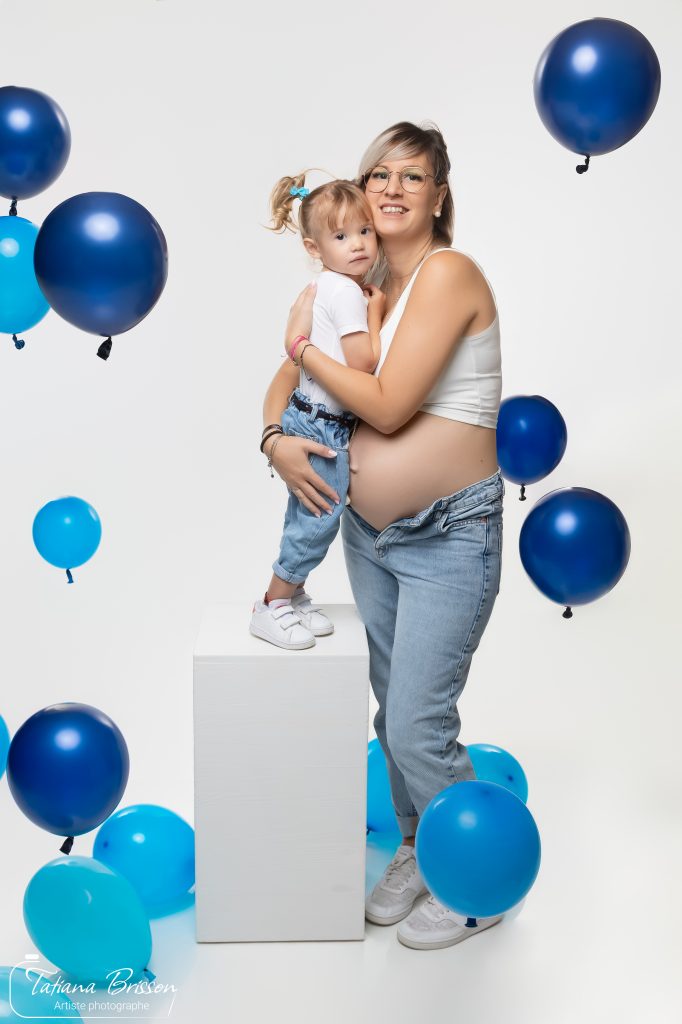 Femme enceinte posant avec sa fille entourées de ballons bleus en studio photo.