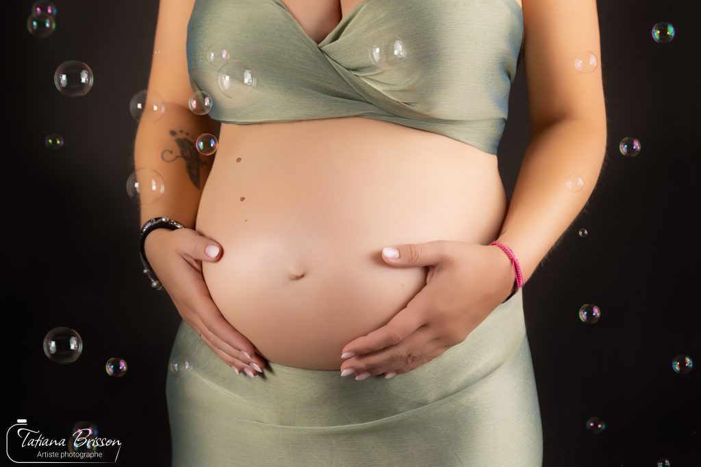Ventre rond de femme enceinte mis en valeur avec des bulles de savon en studio photo.