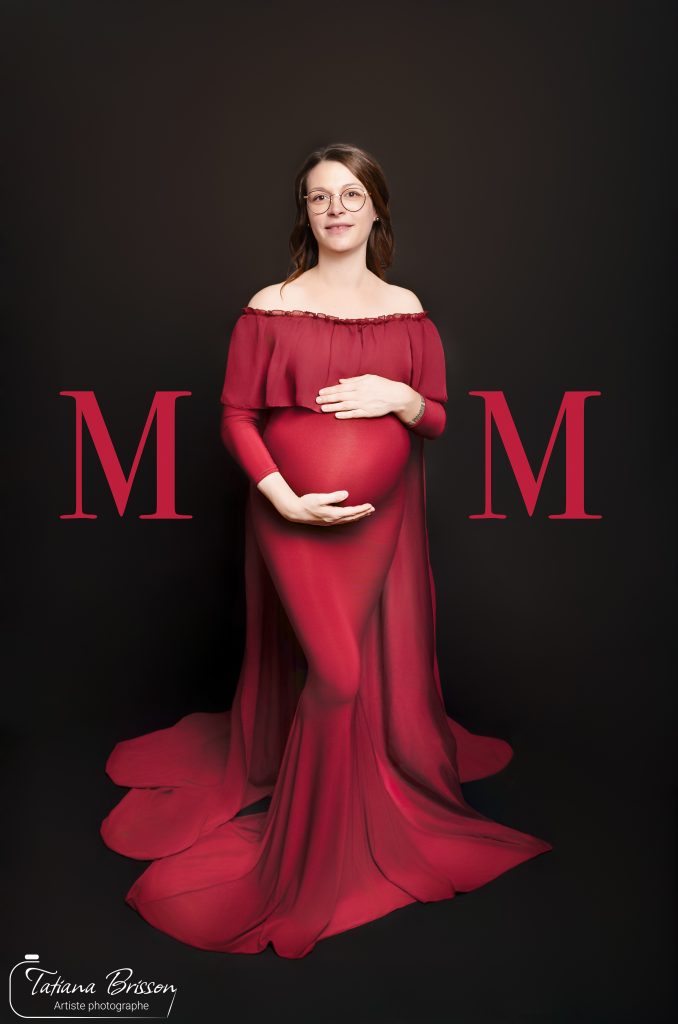 Femme enceinte en robe rouge posant en studio sur fond noir, séance photo grossesse par Tatiana Brisson à Saint-André-d’Huiriat.